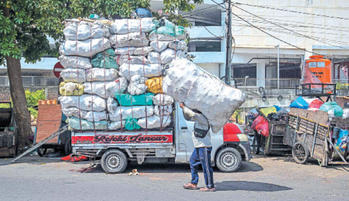 A scavenger carrying a sack of used plastic bottles walks past sacks of disposed household items on a truck in Surabaya, Indonesia on Tuesday. PHOTO: AFP