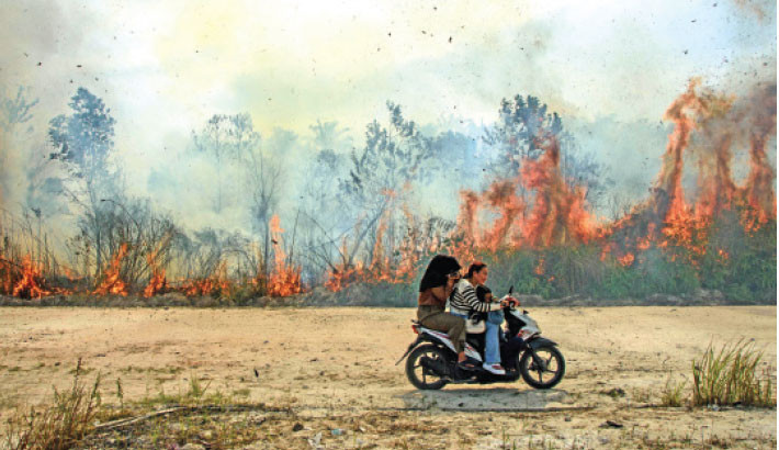 People ride a scooter past a wildfire in Karya Indah, Riau province, Indonesia on Saturday.-AFP PHOTO