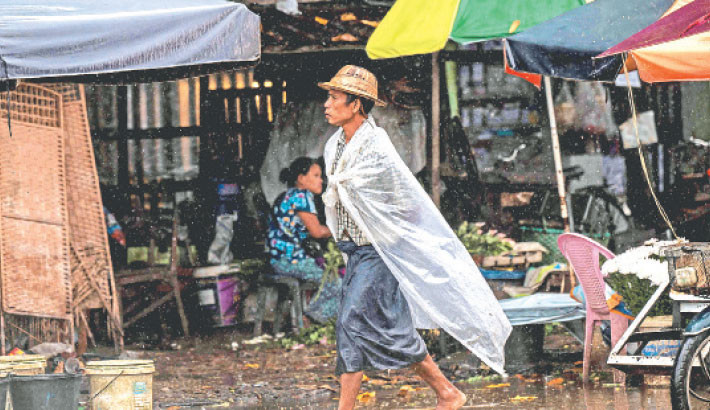 A man wearing a plastic cover to protect himself from the rain walks through a street market in Yangon on 21 July 2025. Photo: AFP