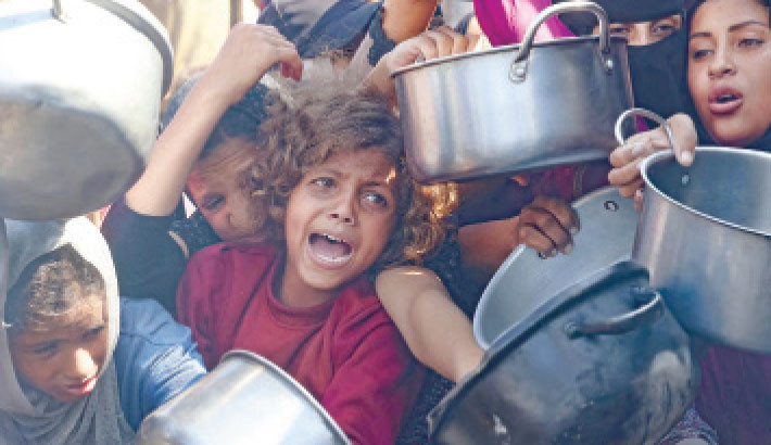 Palestinian women and children hold out their empty pots in front of a charity kitchen in Khan Yunis on Thursday.-AFP PHOTO