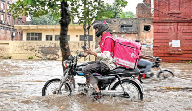 In this photograph taken on 30 August, Abdullah Abbas, a food delivery rider for the Singapore-based company Foodpanda, wades through a flooded street after heavy rainfall in Lahore. Even as monsoon rains deluge Pakistan’s cities killing more than 1,000 people since June, swelling major rivers and devastating rural communities along their banks, food and grocery orders on Foodpanda continue to pour in. - PHOTO: AFP