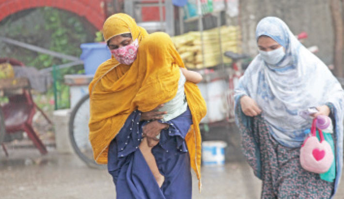 A mother takes her child under her scarf, offering warmth and protection, while another woman weaves her way to work amid a gentle Thursday morning drizzle. The photo was taken in the capital’s Joar Sahara area.  NAZMUL ISLAM
