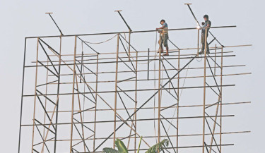 Two workers, without any safety gear, work on a billboard structure in the Amtali area on Mohakhali-Banani Road, exposing themselves to the risk of accidents. The photo was taken on Wednesday.  -  KAMRUL ISLAM RATAN