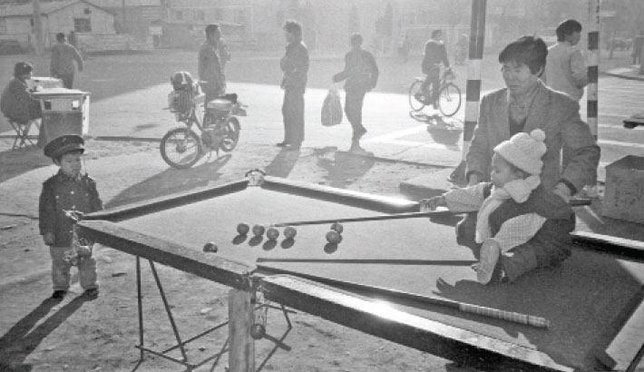 A child sitting on a roadside snooker pool plays with her mother in Beijing in 1983.
